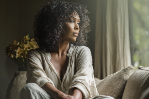Woman sitting quietly in a neutral space, reflecting during a period of feeling stuck